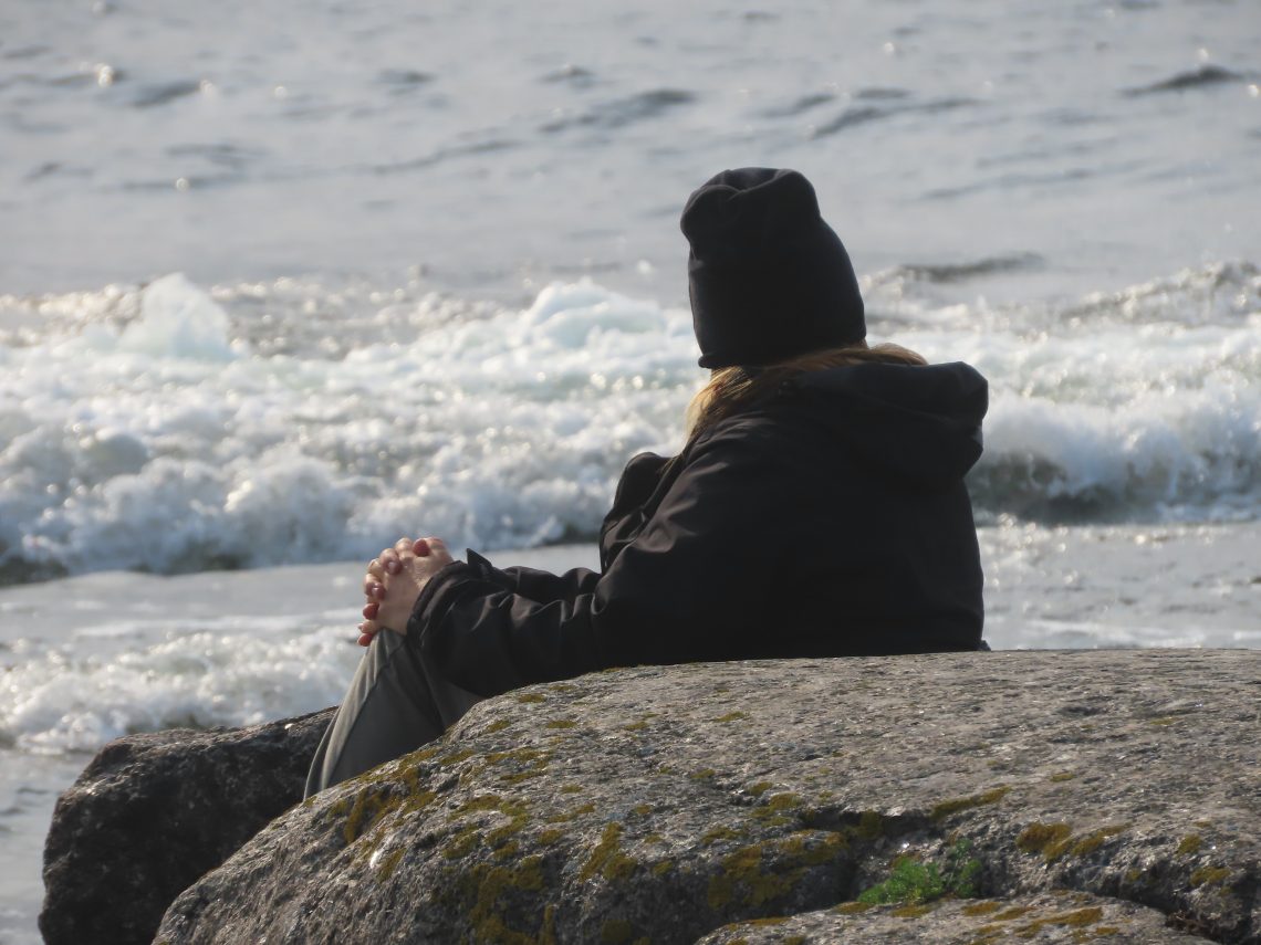 Nainen istuu rannalla