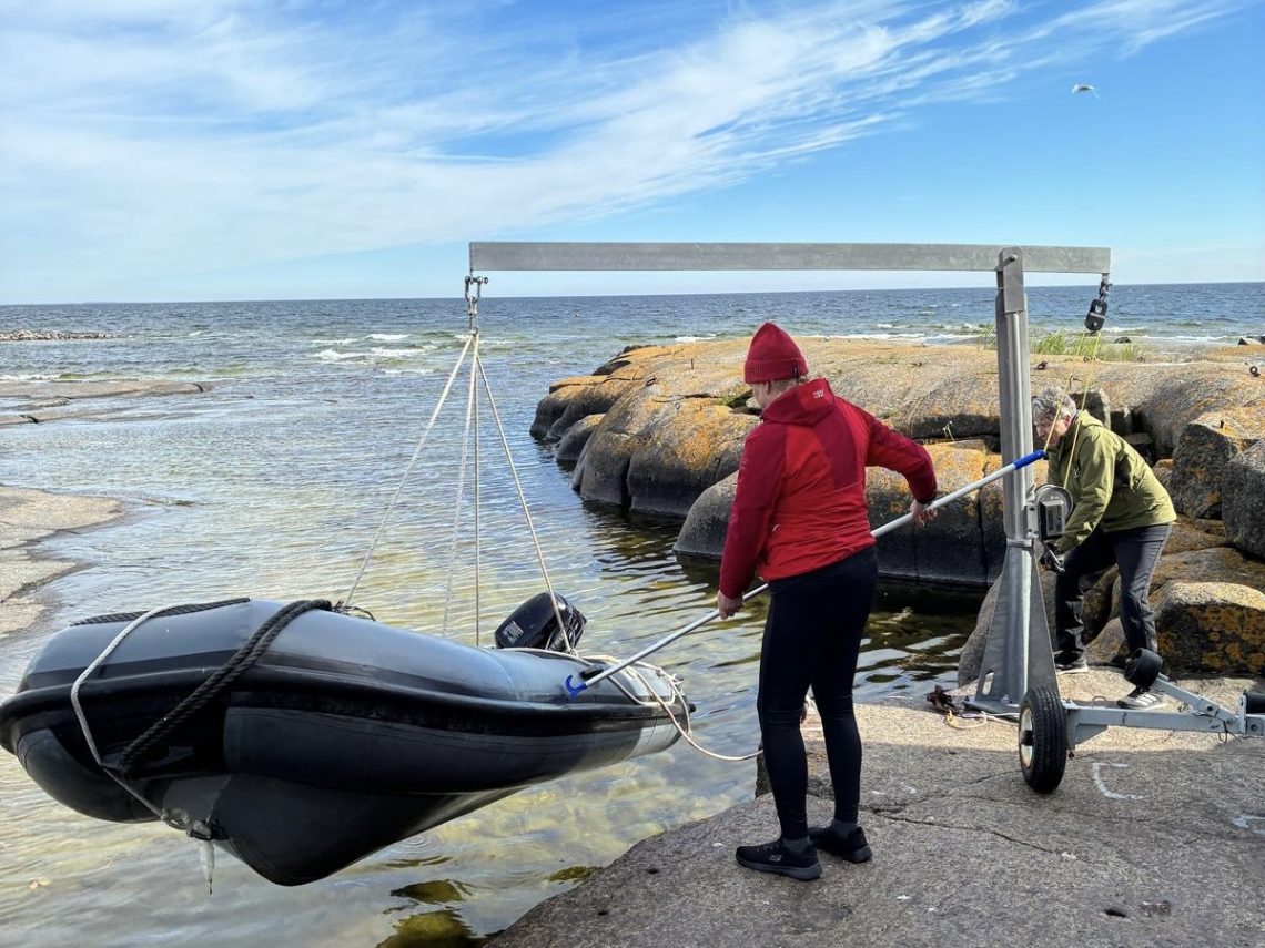 Kaksi talkoolaista nostivat kumiveneen vinssillä ylös sateen varalta.